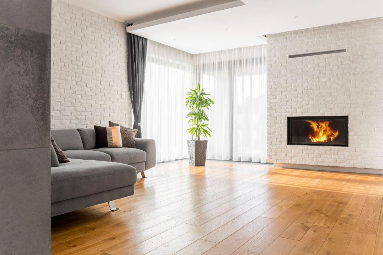 Living room with a grey sofa, white brick walls, a lit fireplace and warm oak floorboards.