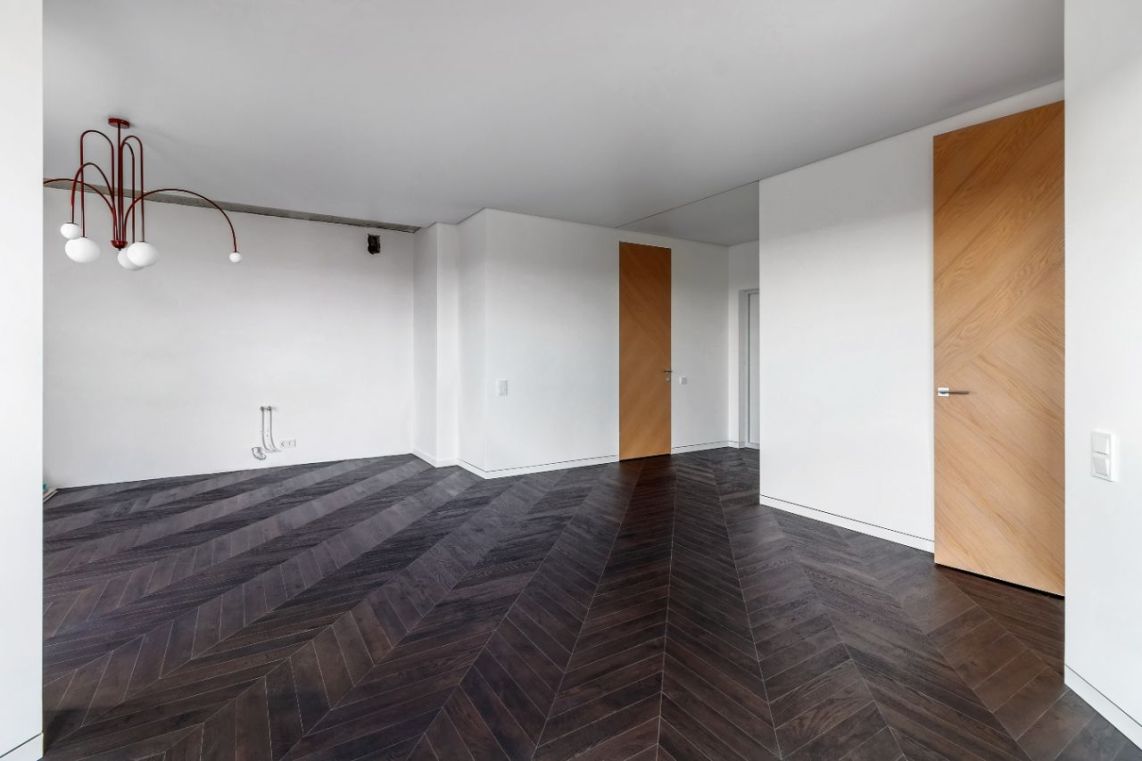 White room with oak doors and dark chevron-pattern wood flooring.