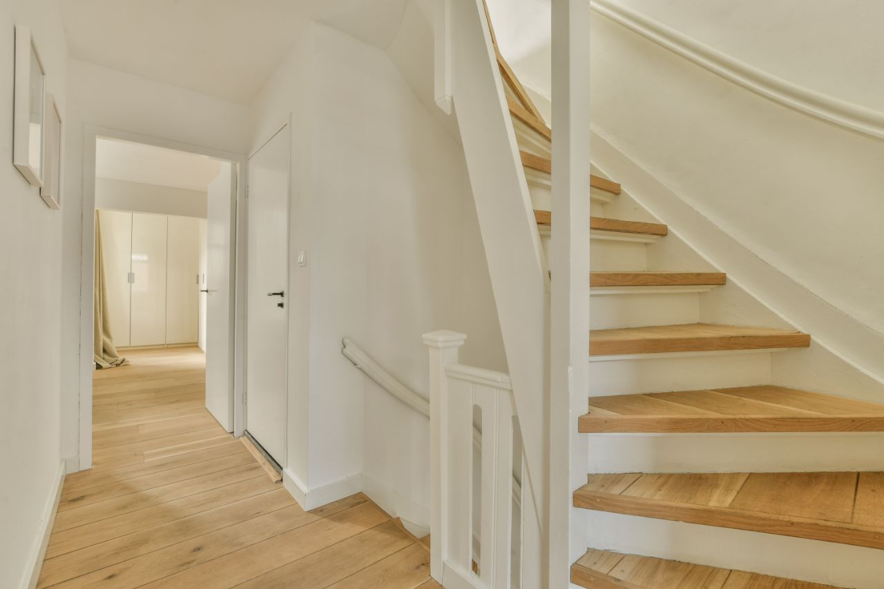 White-painted staircase with oak treads beside a hallway of wide oak floorboards.