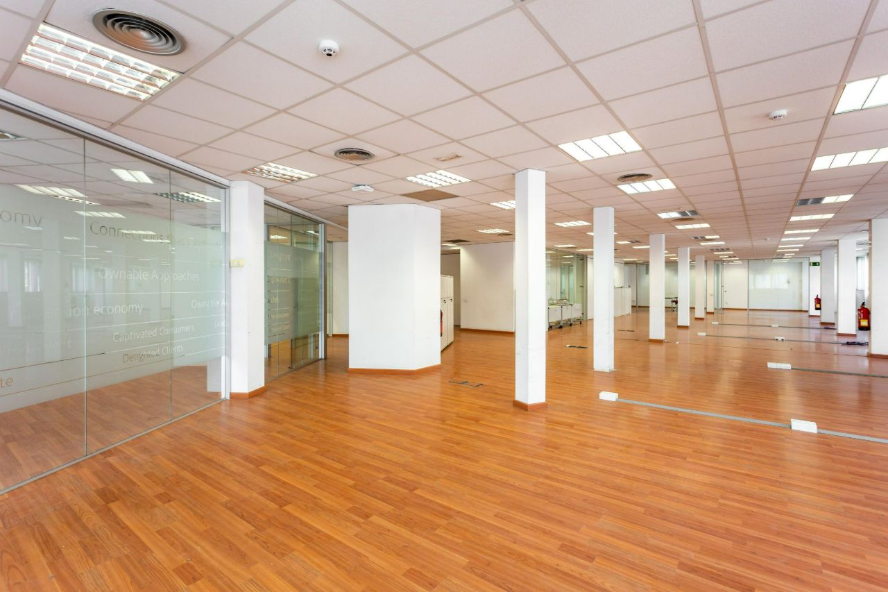 Open-plan office with glass partitions, white columns and a warm brown floor.