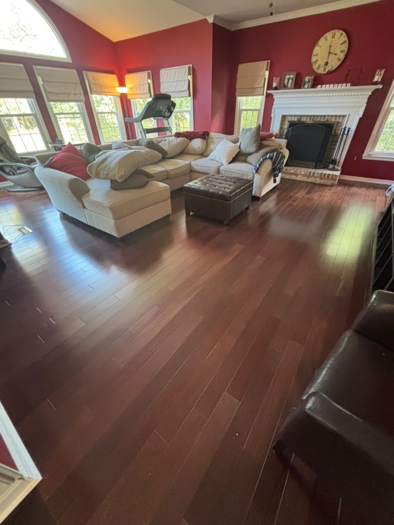 Chestnut Oak solid hardwood by Gold Flooring: deep reddish-brown planks in a living room with red walls, a sectional sofa and a white-mantel brick fireplace