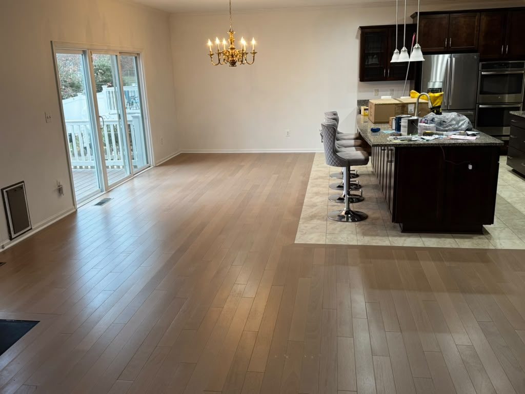 Driftwood solid hardwood by Gold Flooring: light grey-brown planks across an open-plan dining area and kitchen, with sliding doors to a deck and a brass chandelier